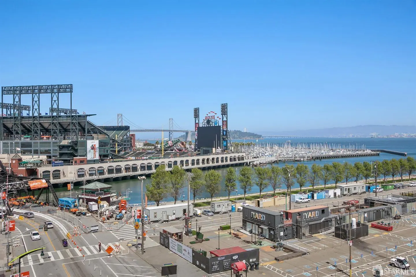 A high-angle view of Oracle Park, the Bay Bridge, and a marina on a sunny day.