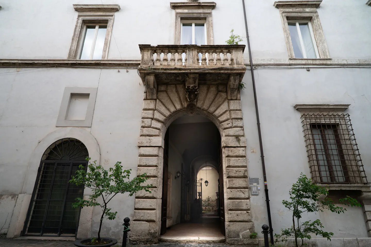 Exterior of a white building with a stone archway leading to a courtyard, windows, and small trees.