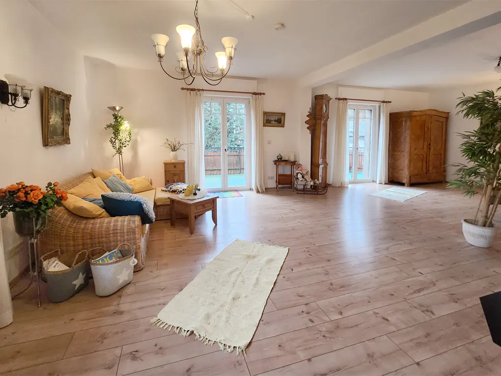 Bright living room with wood floors, wicker sofa with yellow pillows, and a white rug. French doors lead to a balcony.