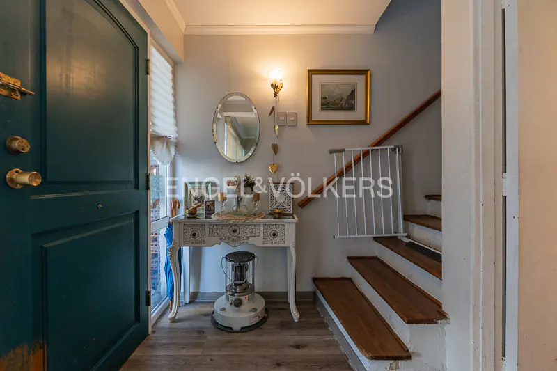Entryway with an open teal door, a white console table with decor, and stairs with a white safety gate. A mirror and framed art hang on the light gray wall.