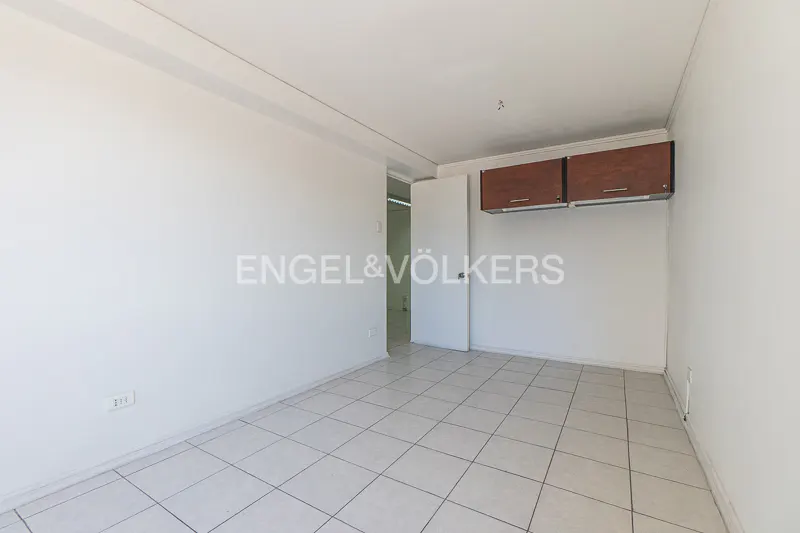 Empty room with white walls, tiled floor, and brown cabinets mounted high on the wall. A doorway is visible in the background.