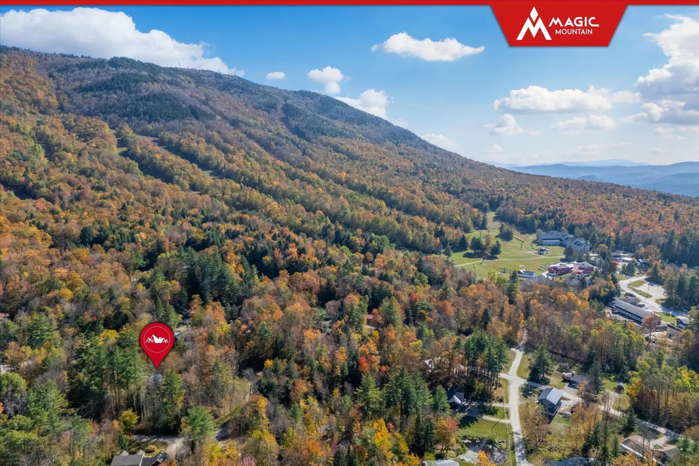Aerial view of Magic Mountain in autumn, with colorful foliage, a red location pin, and a blue sky.