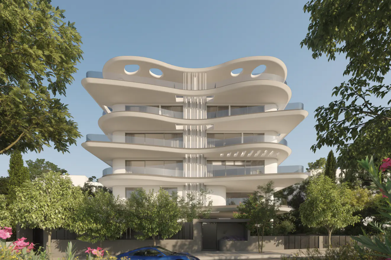 Modern white apartment building with curved balconies and glass railings, surrounded by green trees and a blue car parked in front.