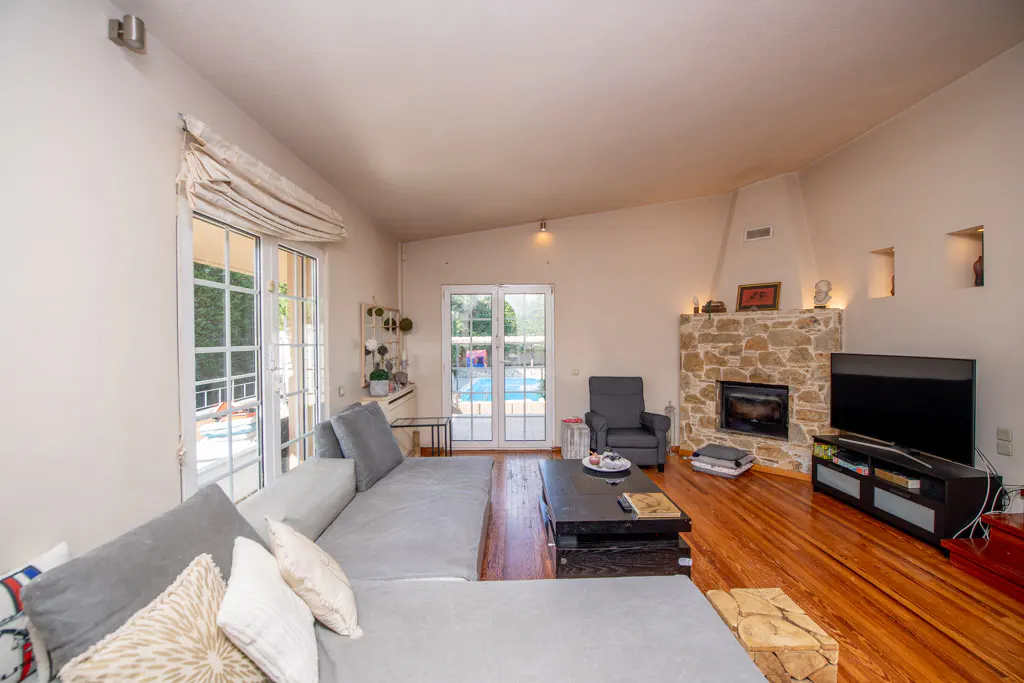 Living room with a gray sectional sofa, stone fireplace, TV, and hardwood floors. French doors lead to a pool.