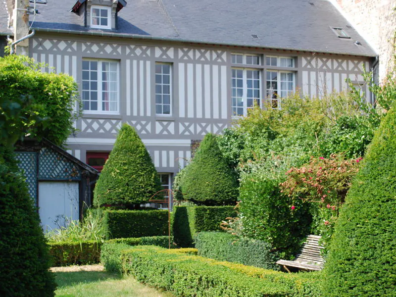 A two-story house with a gray roof and white and gray siding, surrounded by a green garden with trimmed bushes.