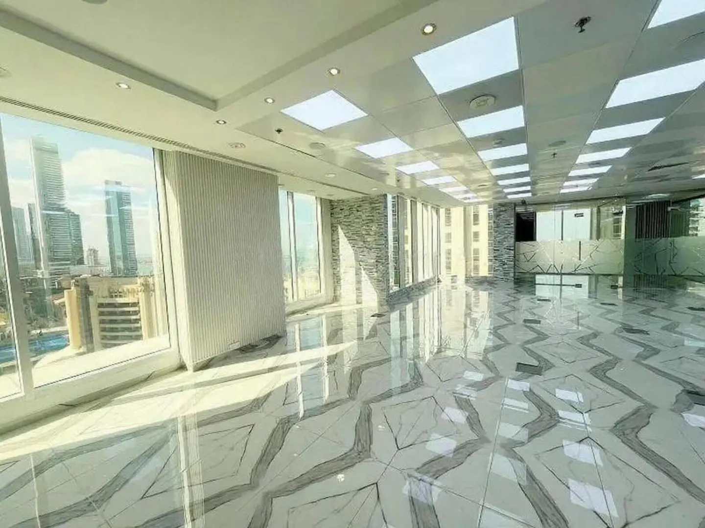 Bright, empty office space with marble floors, large windows, and a city view.