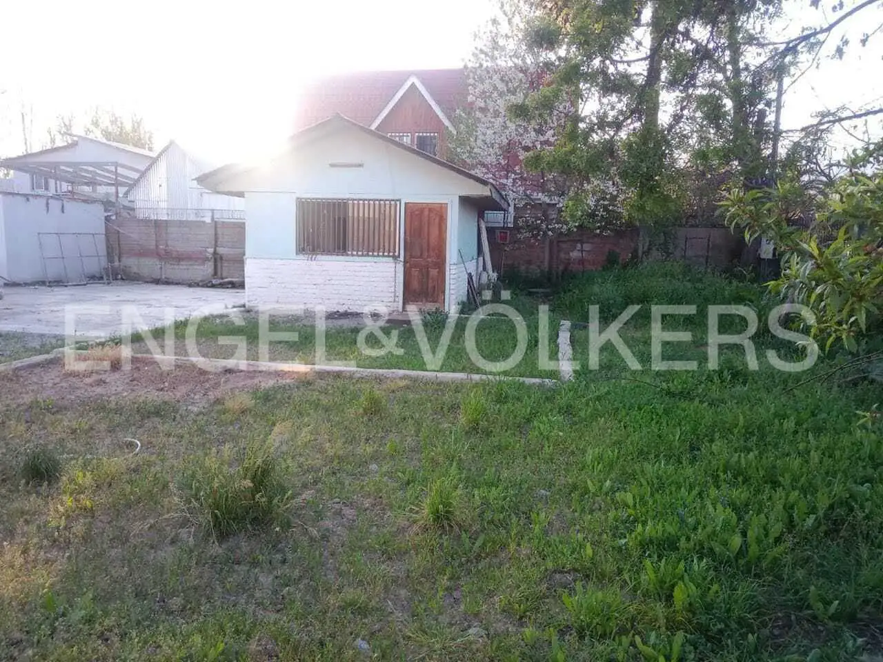 A light blue shed with a brown door sits on a grassy lot, with a house and trees in the background.