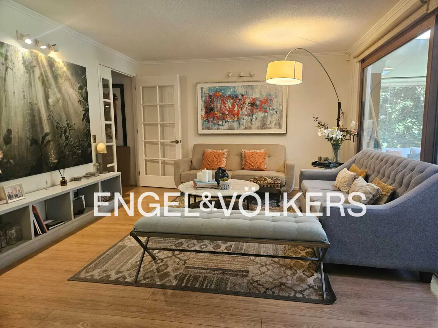Living room with hardwood floors, a gray sofa, a beige sofa, and a bench on a patterned rug. Artwork adorns the walls.
