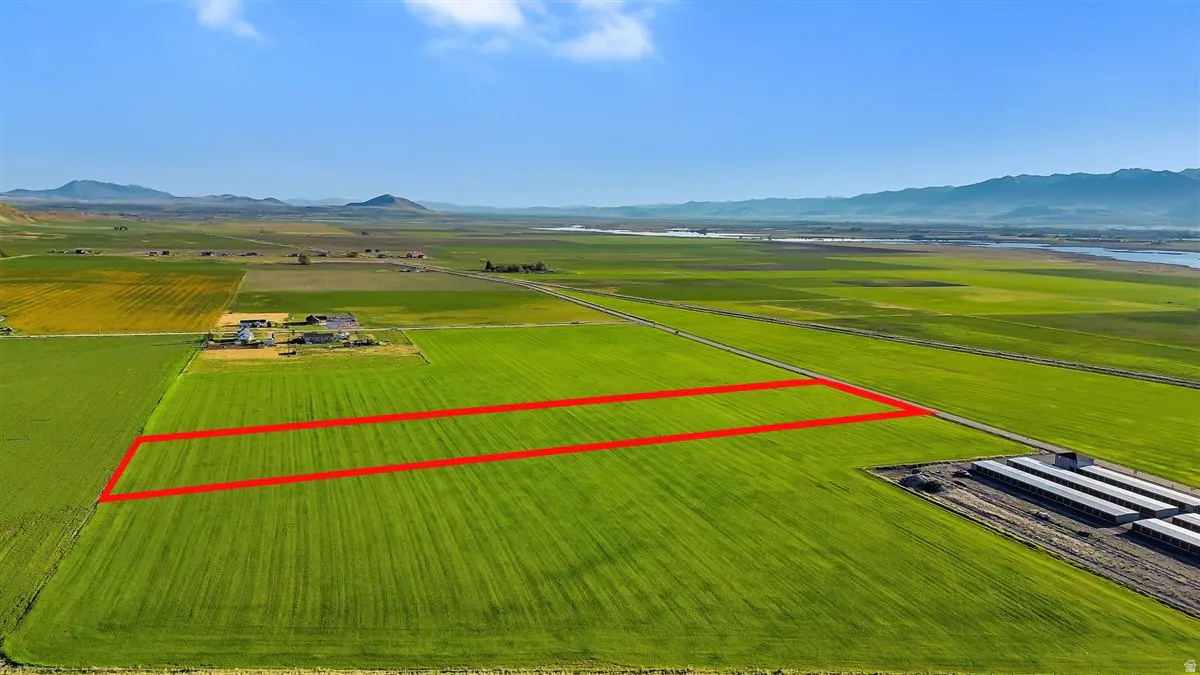 Aerial view of a green field outlined in red, with mountains and a blue sky in the background.