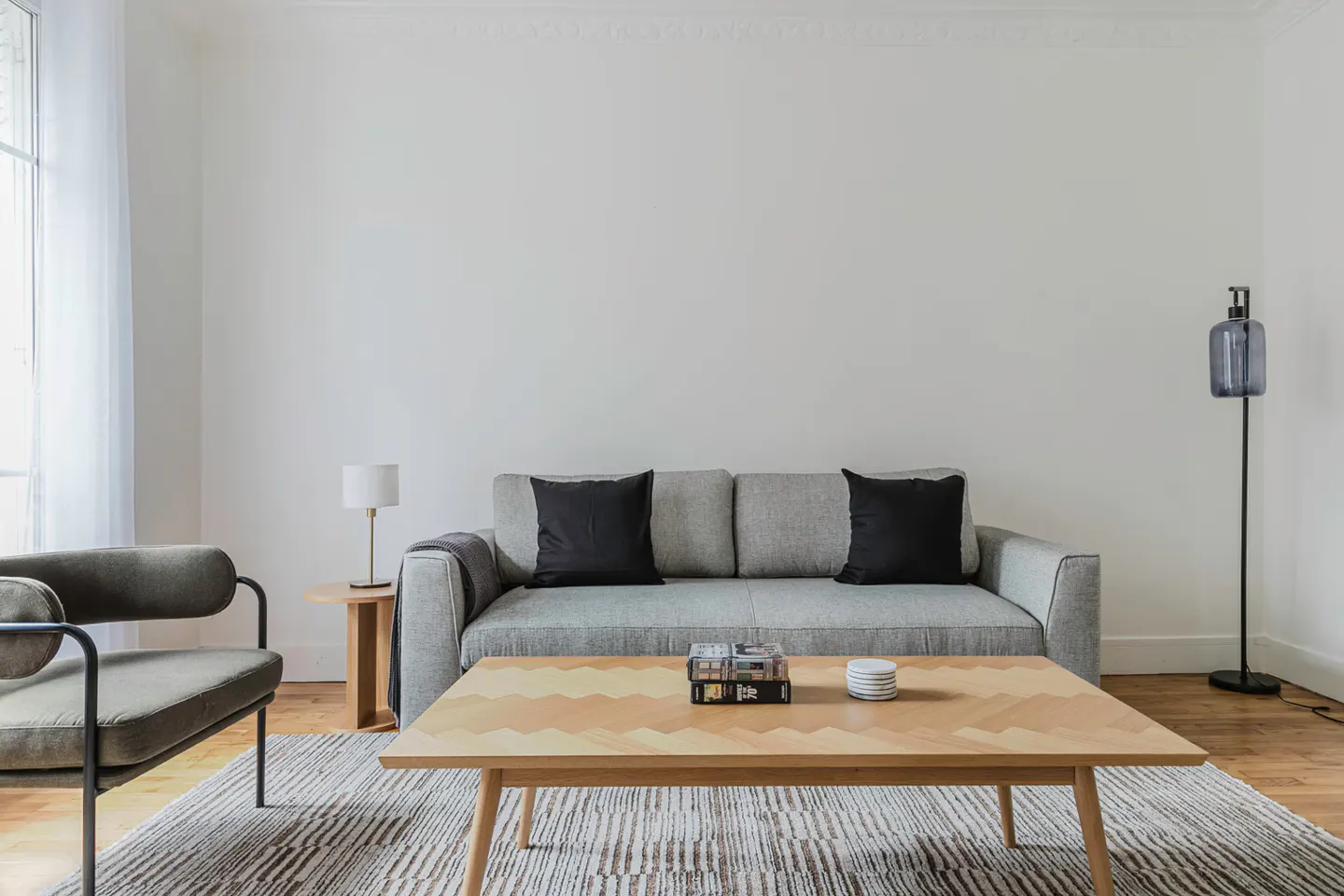Living room with gray sofa, black pillows, patterned wood coffee table, and gray chair on a striped rug.