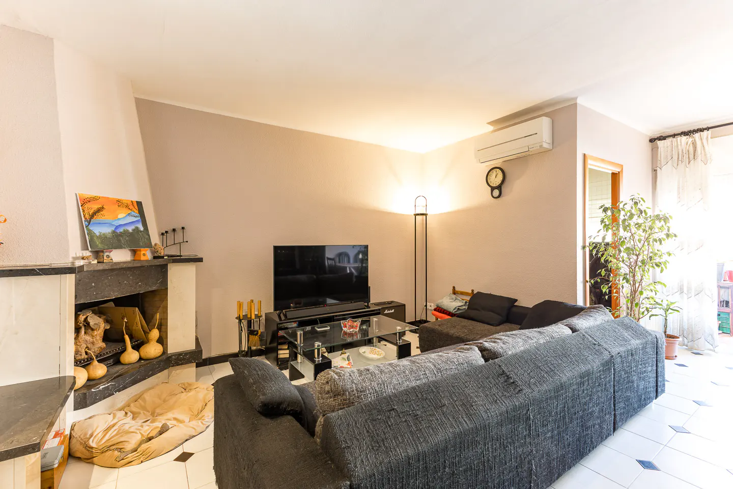 A living room with a gray sofa, fireplace, TV, and glass coffee table. A painting hangs above the fireplace.