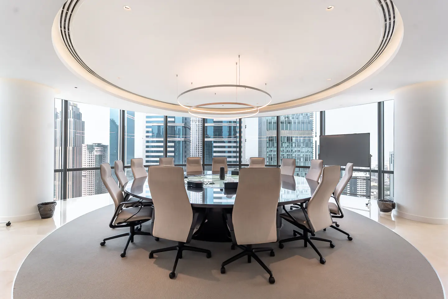 Bright, modern conference room with a round table, beige chairs, and a city view through large windows.