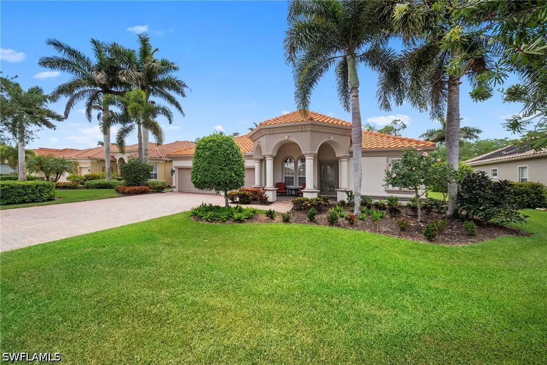 Beige single-story house with a red tile roof, white columns, and palm trees under a blue sky.