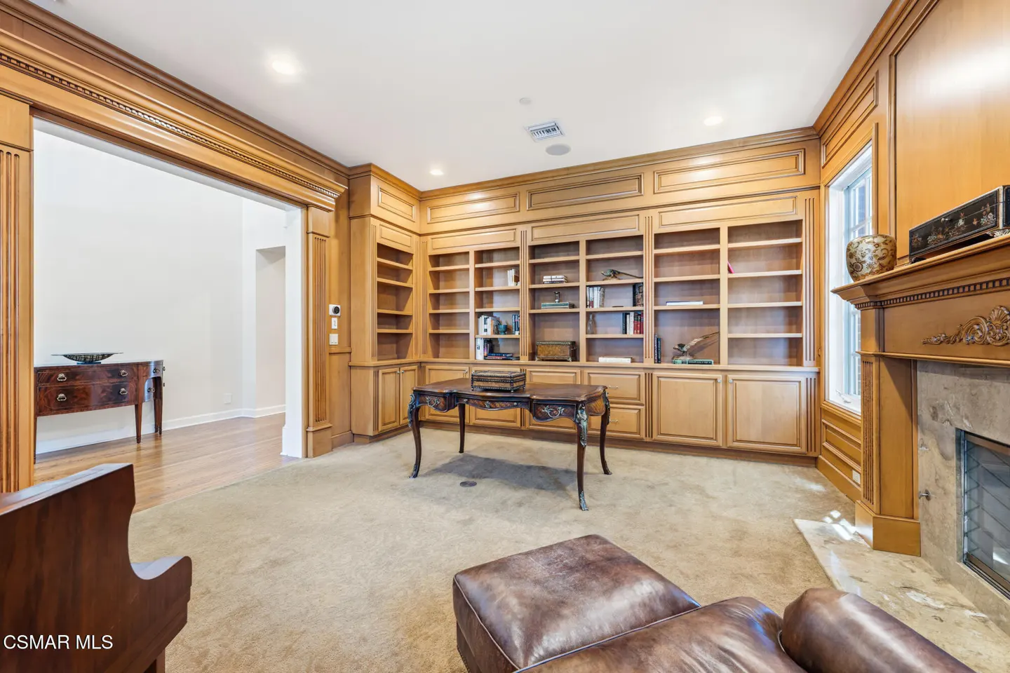 A home office with wood paneling, built-in bookshelves, a desk, and a fireplace.
