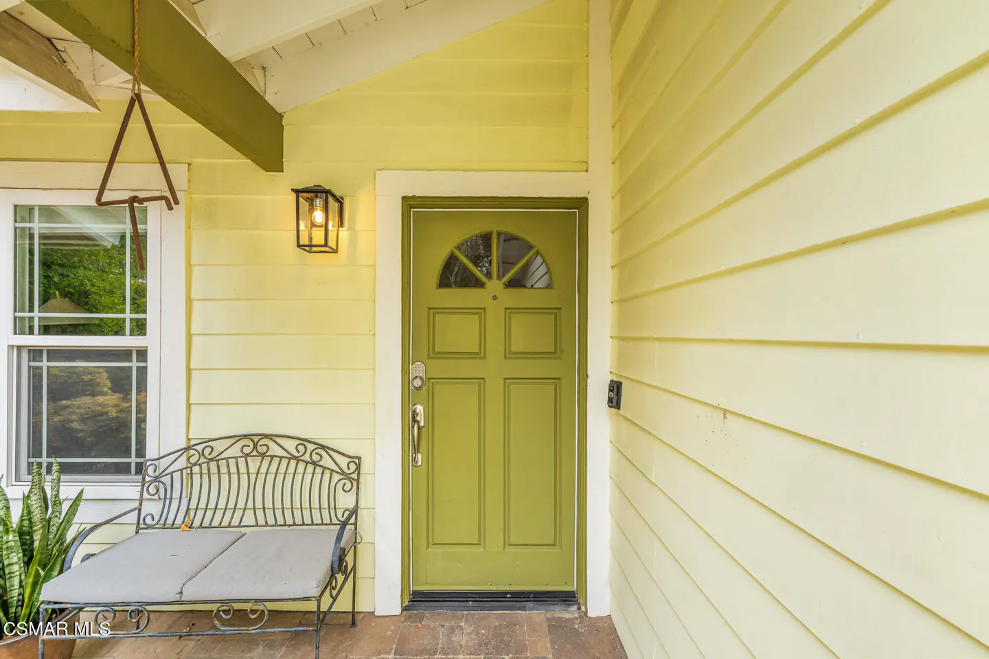 Exterior of a yellow house with a green front door, a bench, and a window.