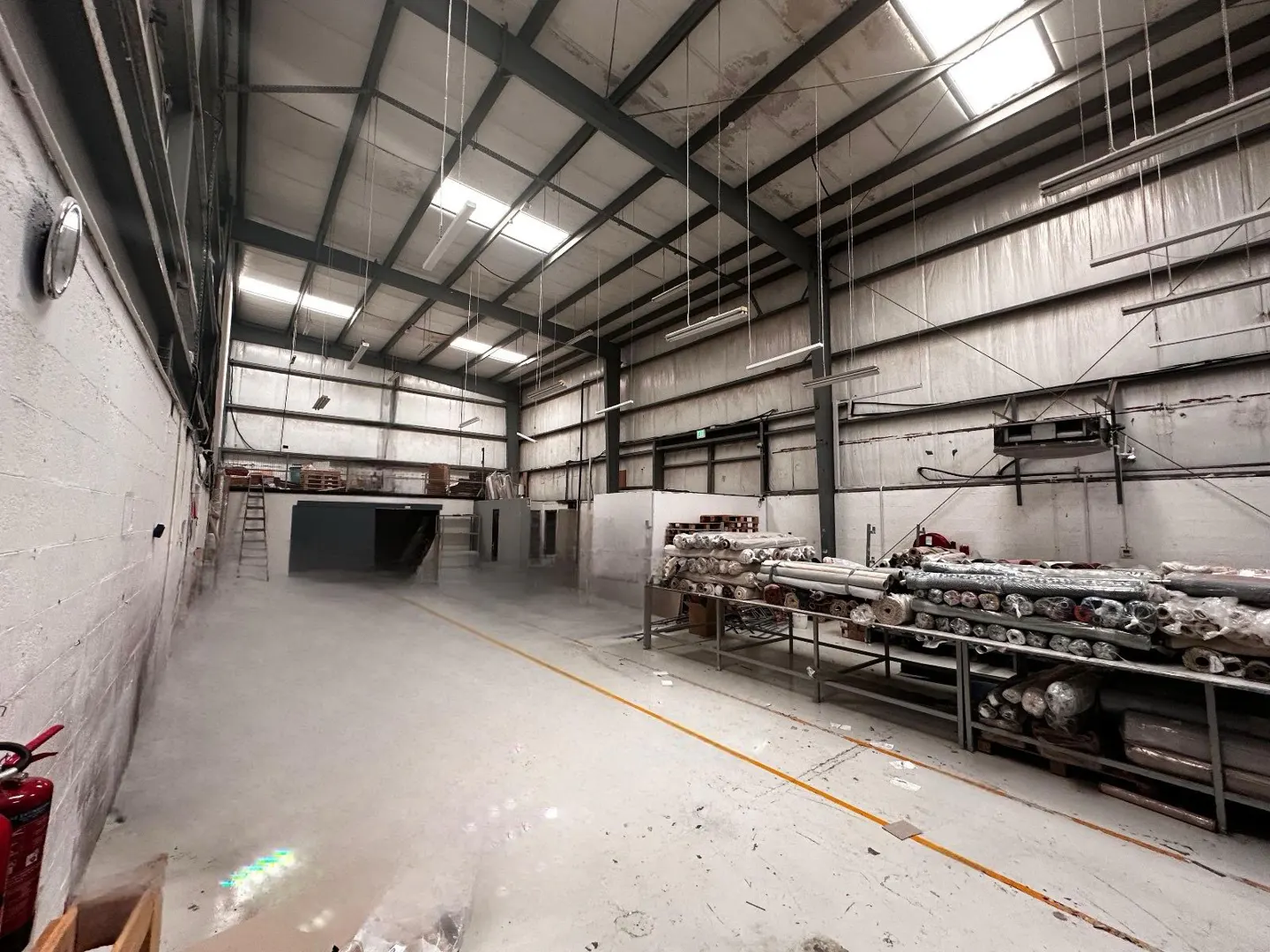 A wide shot of a large, empty warehouse with rolls of carpet on shelves to the right.