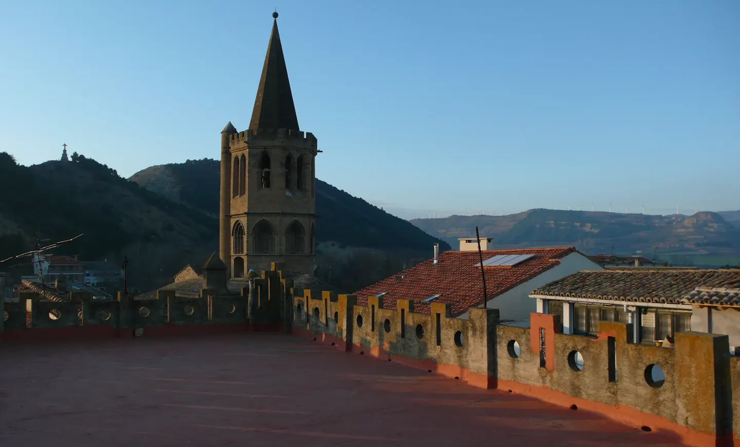 View from a rooftop with a stone wall, a church tower, and mountains in the background.