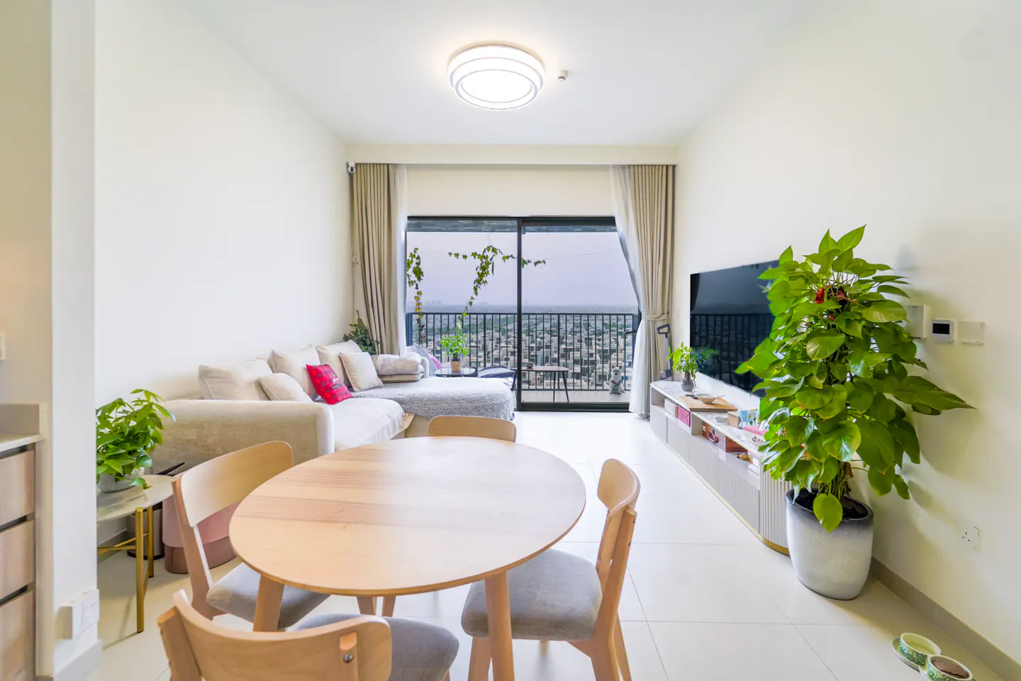 Bright living room with a round wooden table and four chairs, a white sofa, and a large window with a city view.