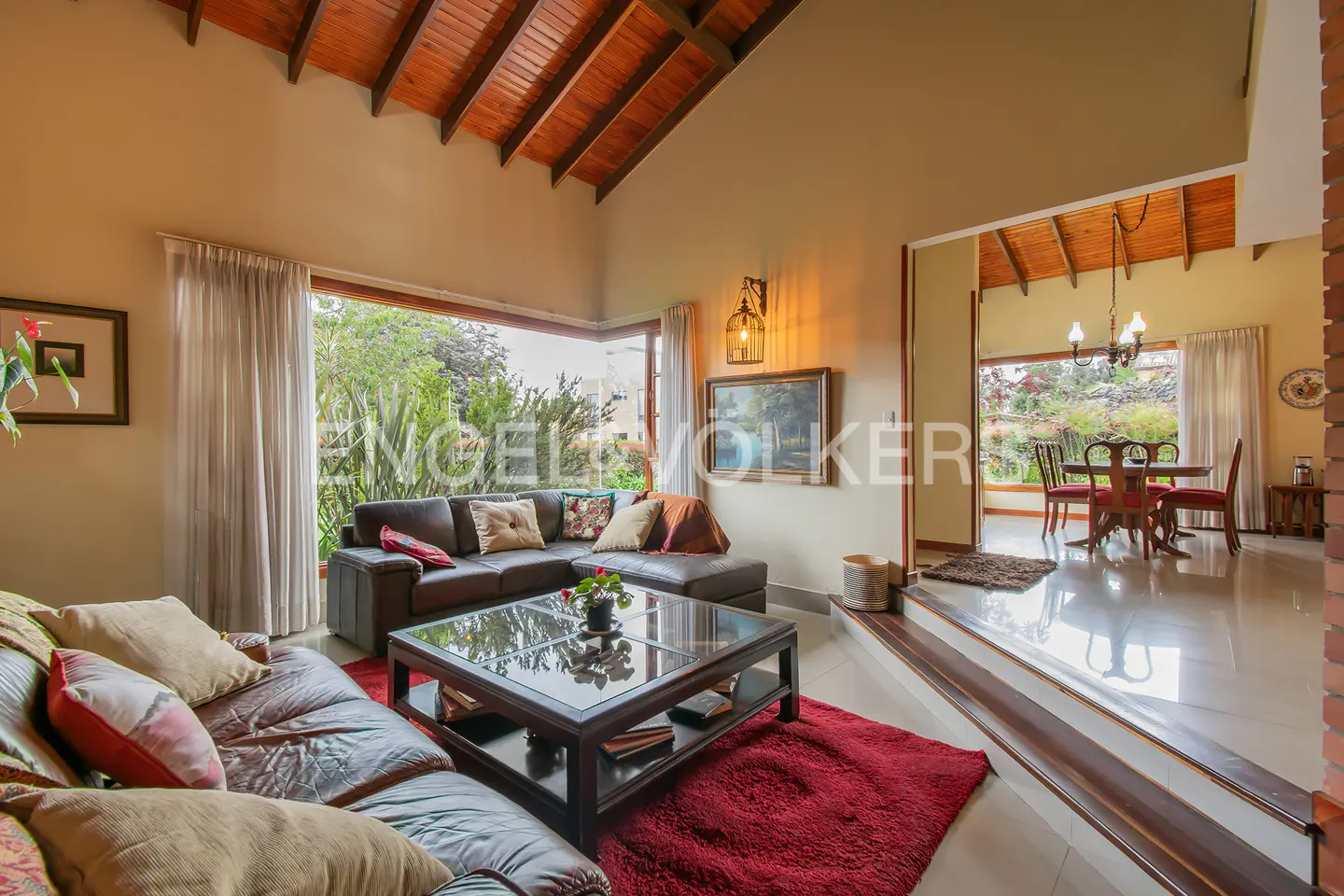 Living room with brown leather sofas, a glass coffee table, and a red rug. Dining room with table and chairs in the background.