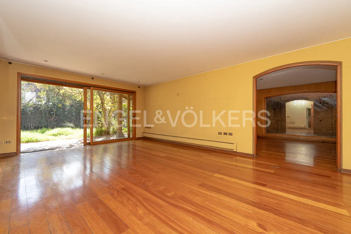 Empty living room with yellow walls, wood floors, and a sliding glass door to a green yard. An arched doorway leads to another room.