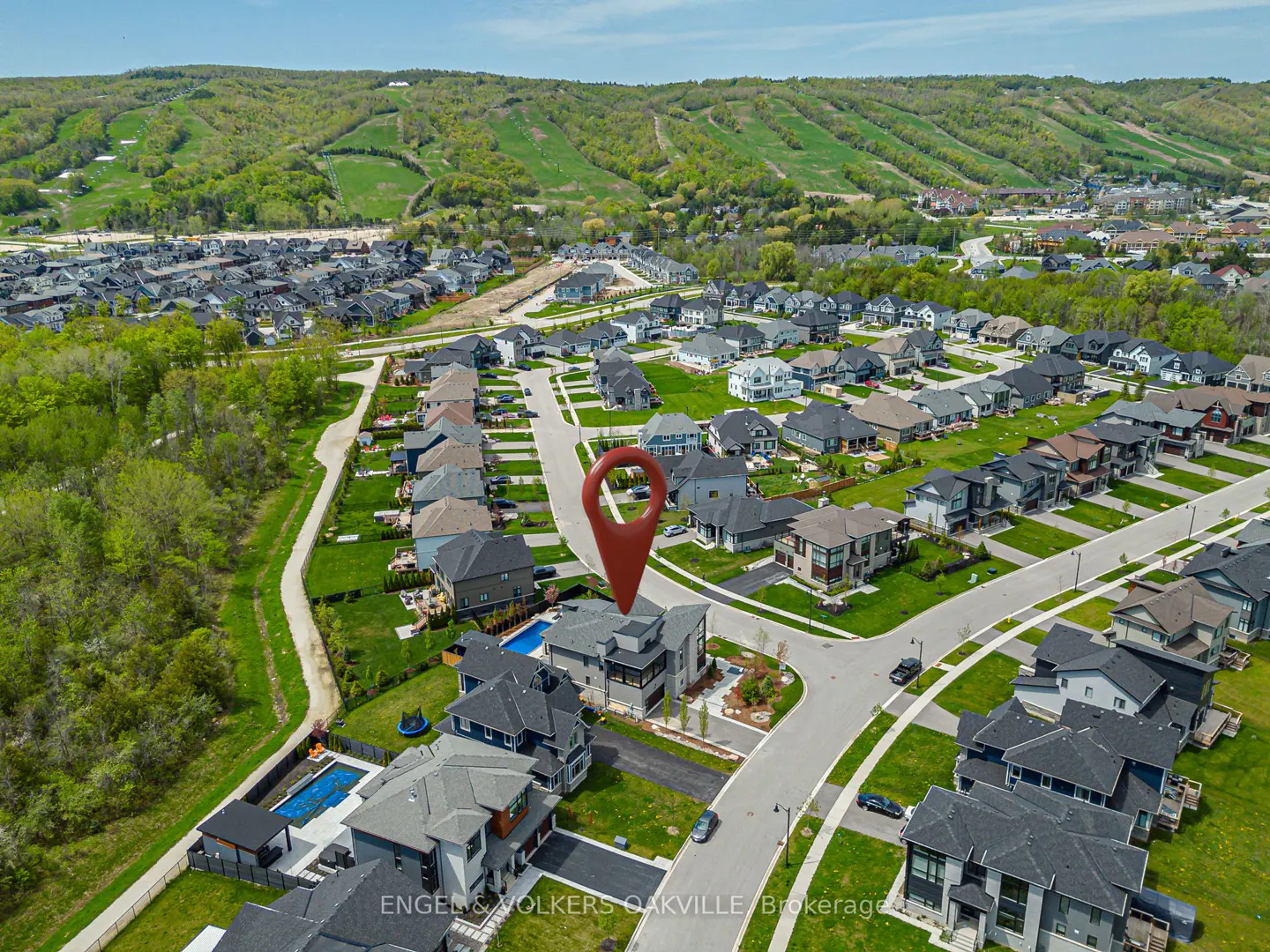 Aerial view of a modern home with a red location pin, in a suburban neighborhood with green hills in the background.