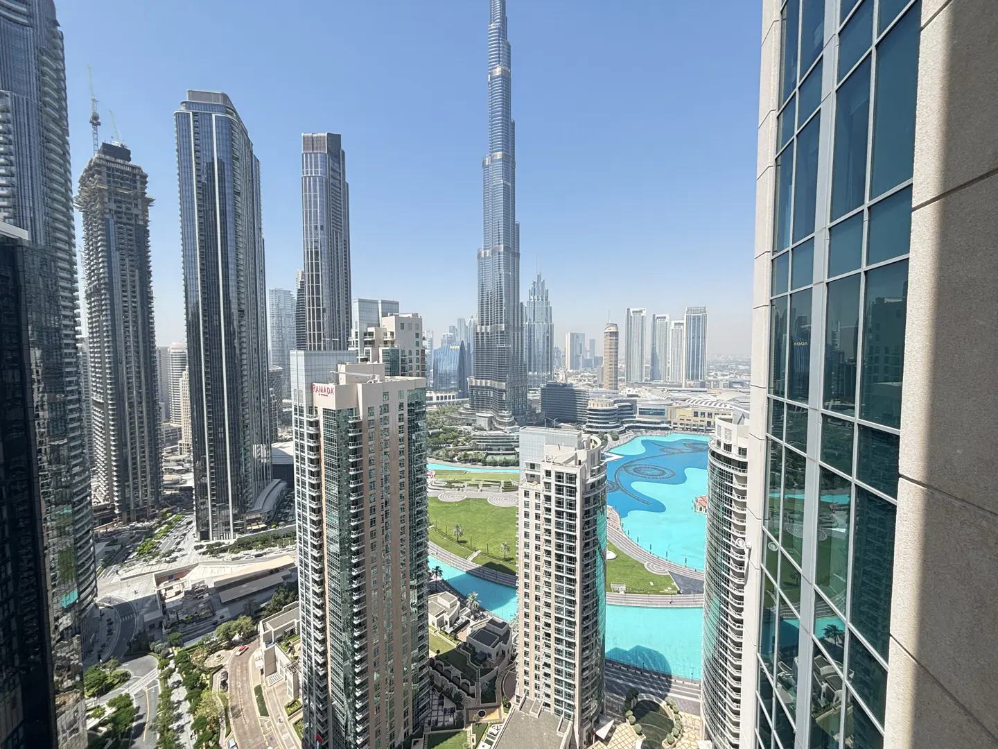 View of Dubai skyline featuring the Burj Khalifa, skyscrapers, and a large turquoise water feature.