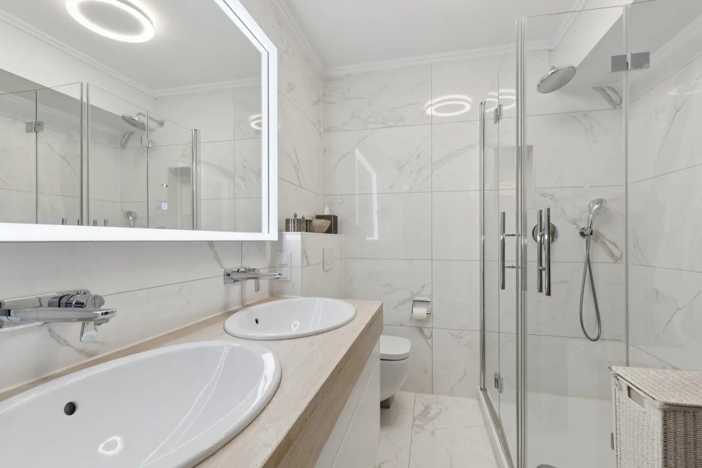 Bright, modern bathroom with marble tile, double sinks, and a glass-enclosed shower.