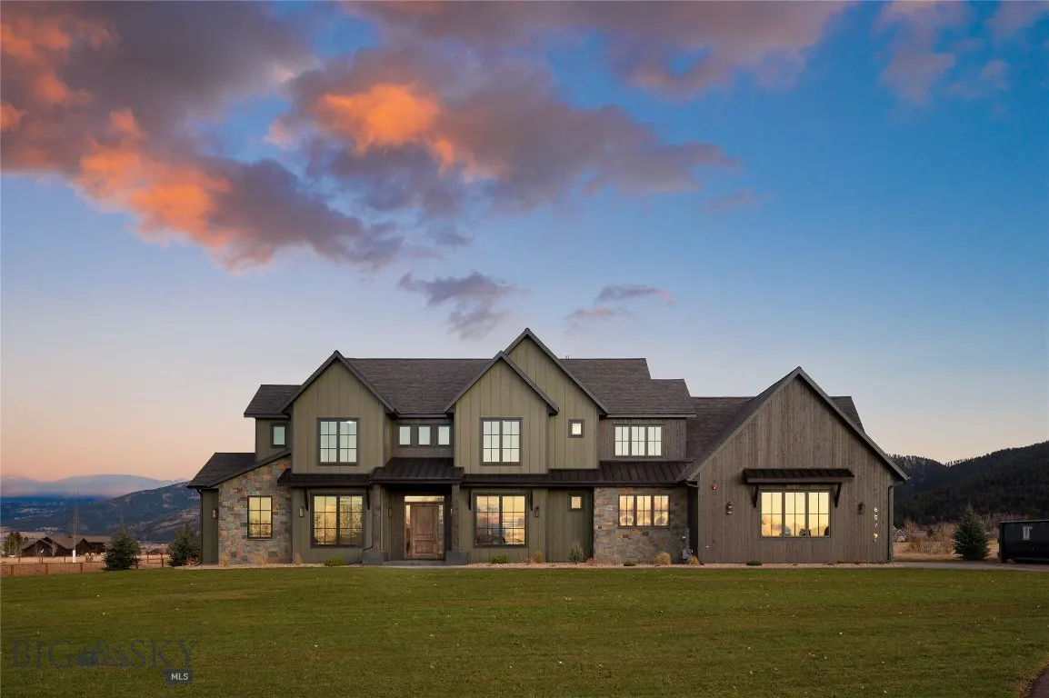 Two-story house with green siding and stone accents, set on a green lawn under a colorful sunset sky.