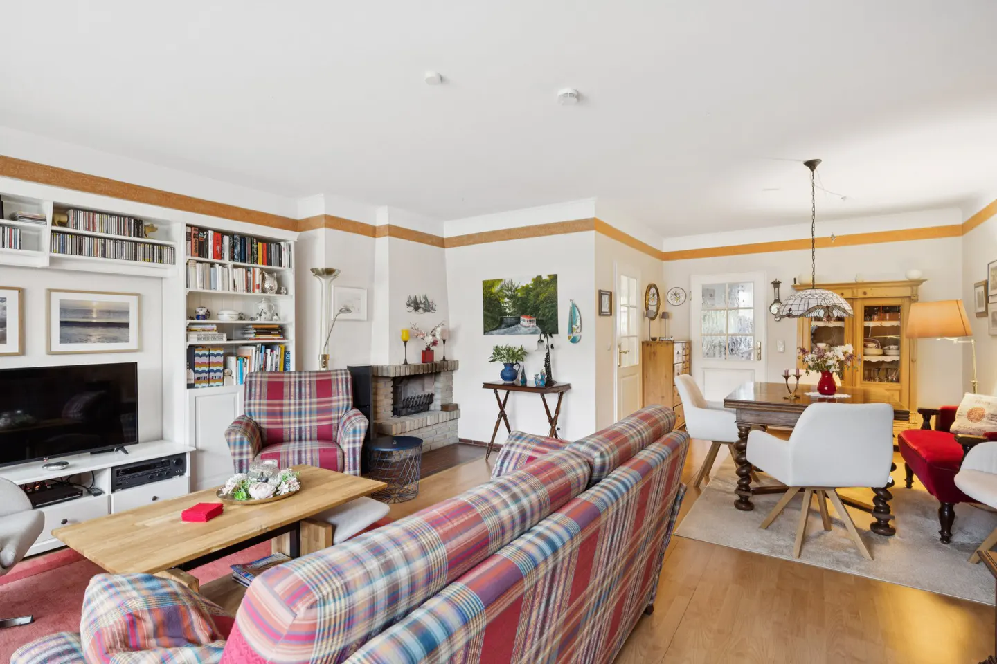 A living and dining room with a plaid sofa, fireplace, and built-in bookshelves.