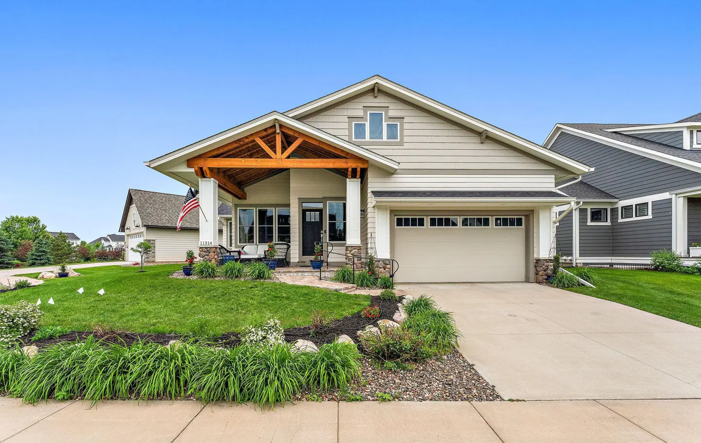 Beige single-story house with a front porch, green lawn, and a driveway leading to an attached garage.