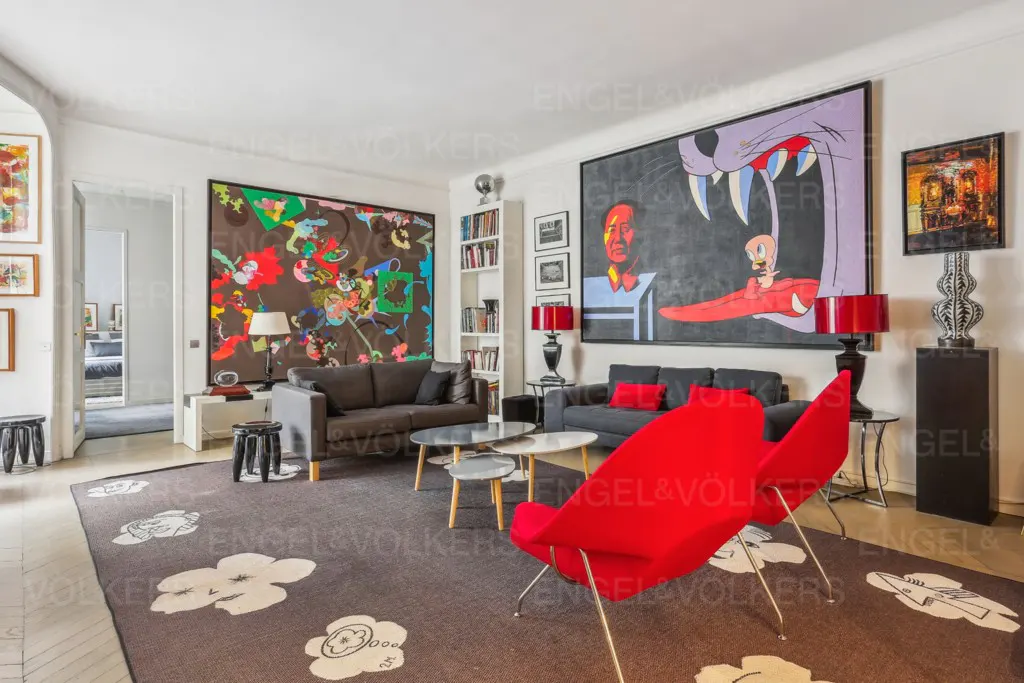 A living room with two sofas, red chairs, and large art pieces. The rug is brown with white flower designs.