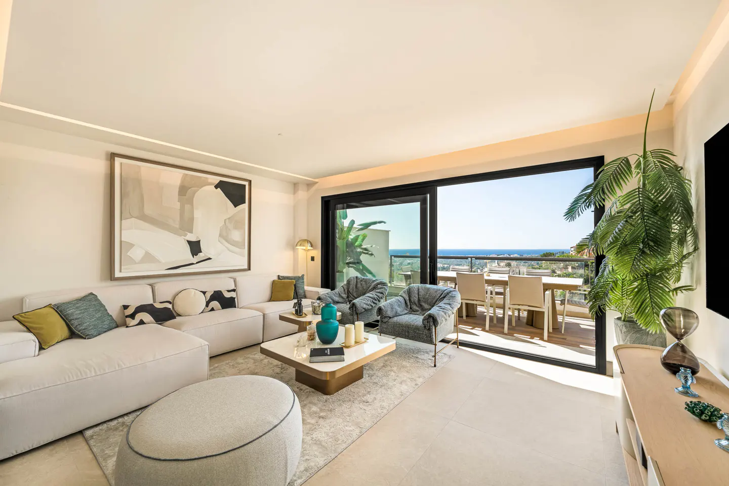 Bright living room with white sofa, two gray chairs, and a marble coffee table. Sliding glass doors open to a balcony with ocean views.