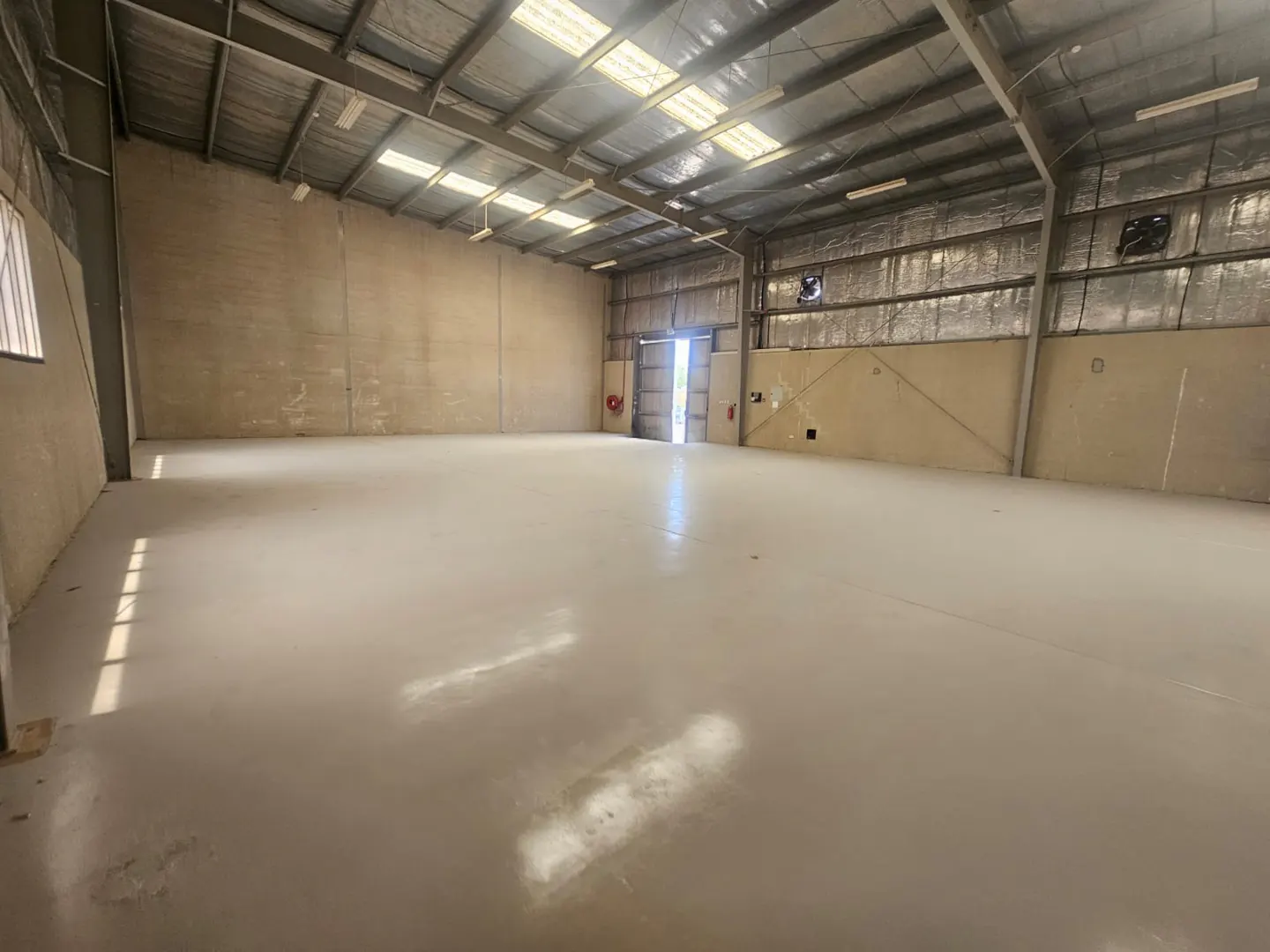 A large, empty warehouse with a concrete floor and metal walls and ceiling. An open door is visible at the far end.
