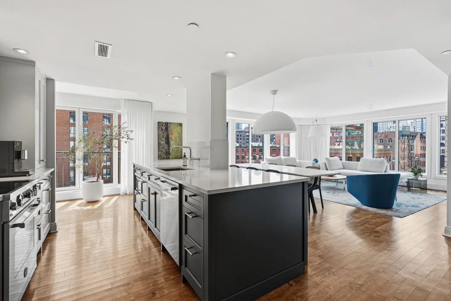 Open-concept kitchen and living room with hardwood floors and city views. A dark island anchors the kitchen.