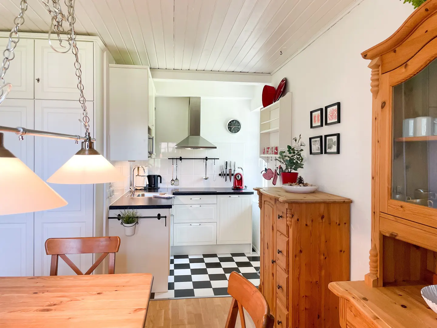 A bright kitchen with white cabinets, black countertops, and black and white checkered floors. A wooden table and chairs are in the foreground.