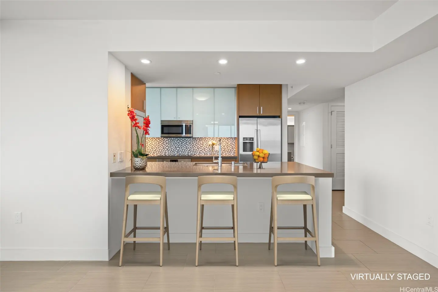 A bright, modern kitchen with light blue and wood cabinets, stainless steel appliances, and a gray countertop with three wooden bar stools.