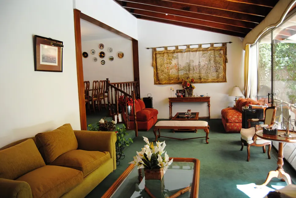 A living room with green carpet, a brown couch, a tapestry on the wall, and a view of a staircase and dining room.