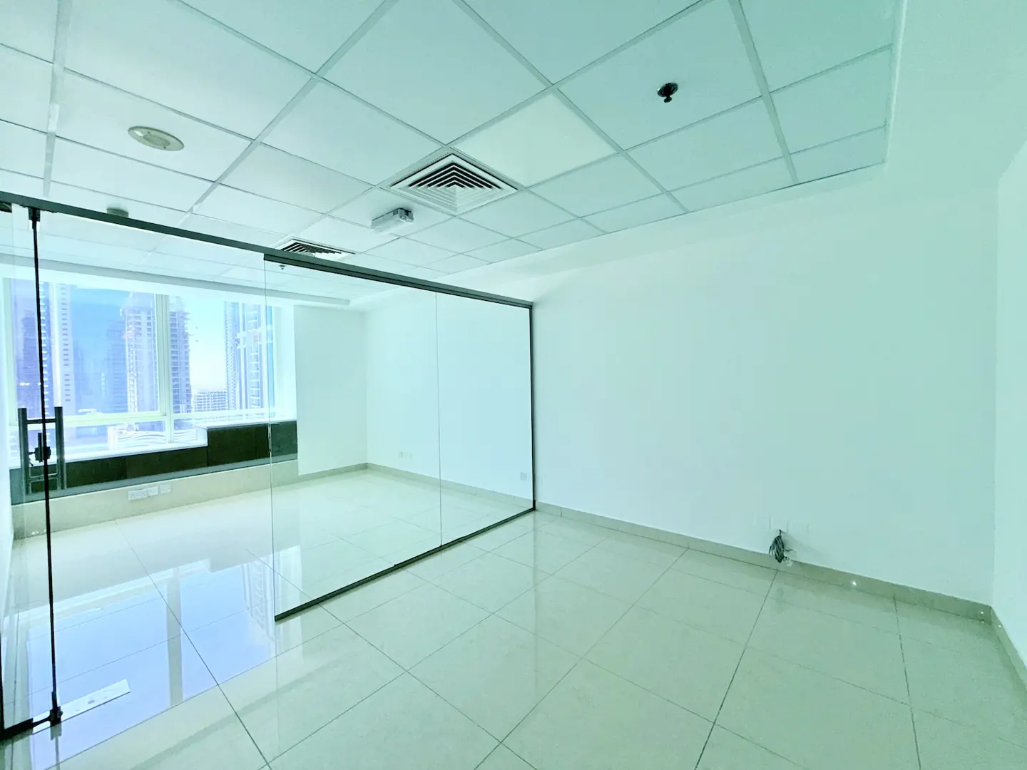 Empty office space with white walls, tiled floor, and a glass-walled room overlooking a city skyline.