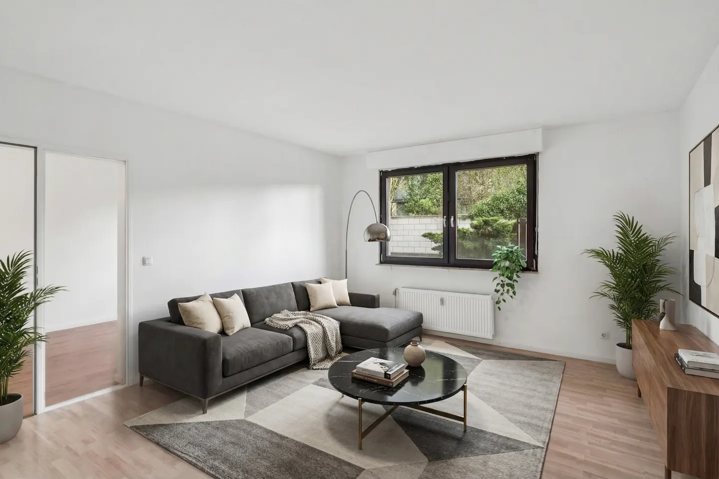 Bright living room with gray sectional sofa, marble coffee table, patterned rug, and large window overlooking greenery.