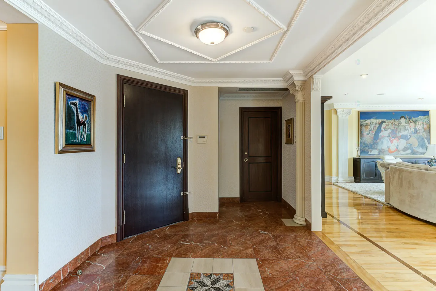 A home's foyer with marble floors, a dark wood door, and a painting on the wall. A second door is visible in the background.