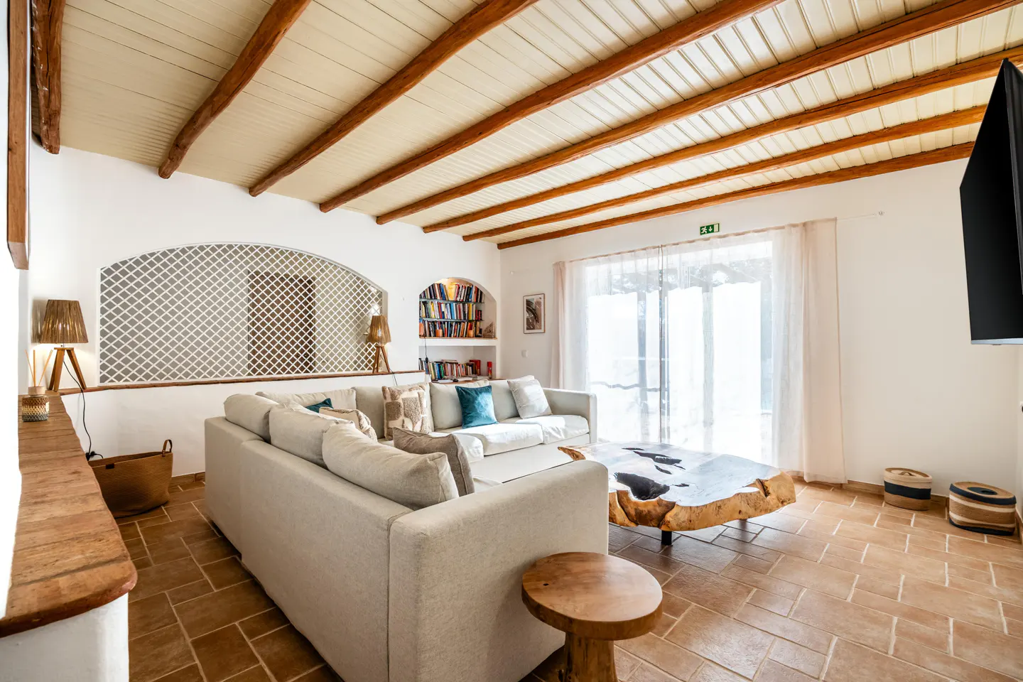 Living room with white sofas, a wooden coffee table, and terracotta tile floors. White walls and a beamed ceiling add to the room's charm.