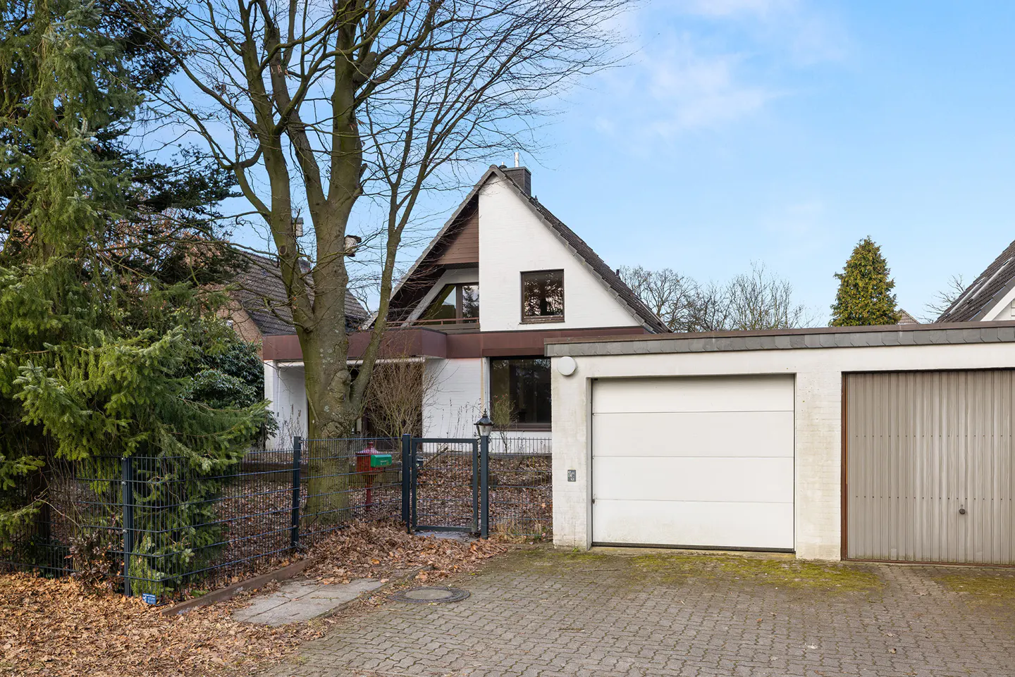 Exterior of a white, A-frame house with a two-car garage and a black metal fence.