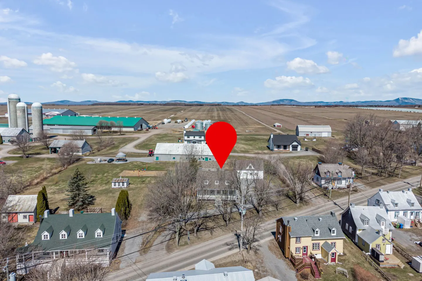 Aerial view of a rural area with houses, farms, and a red location pin over a house.
