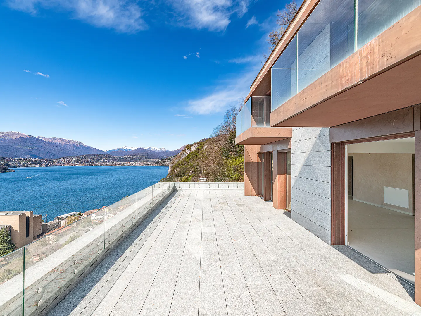 Modern home with a large patio overlooking a blue lake and mountains under a clear blue sky.
