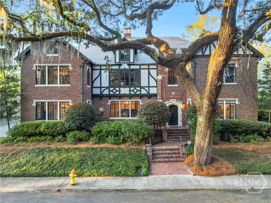 Two-story brick house with white trim and a large tree in front. A yellow fire hydrant is on the sidewalk.