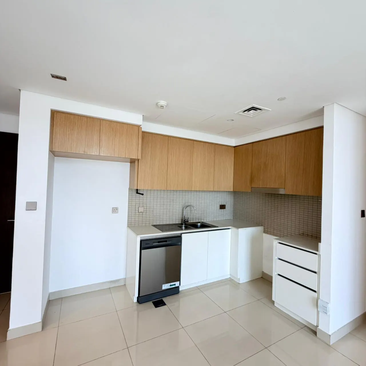 A bright, modern kitchen with light wood cabinets, white countertops, and stainless steel appliances.
