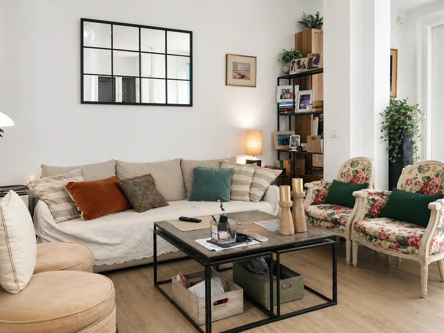 Living room with a beige sofa, floral armchairs, and a black-framed mirror on a white wall. A metal coffee table sits in the center.