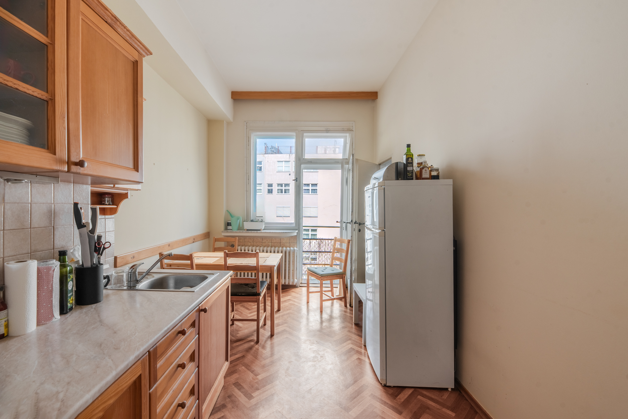 Narrow kitchen with wooden cabinets, a white refrigerator, a small dining table, and a balcony door with city views.