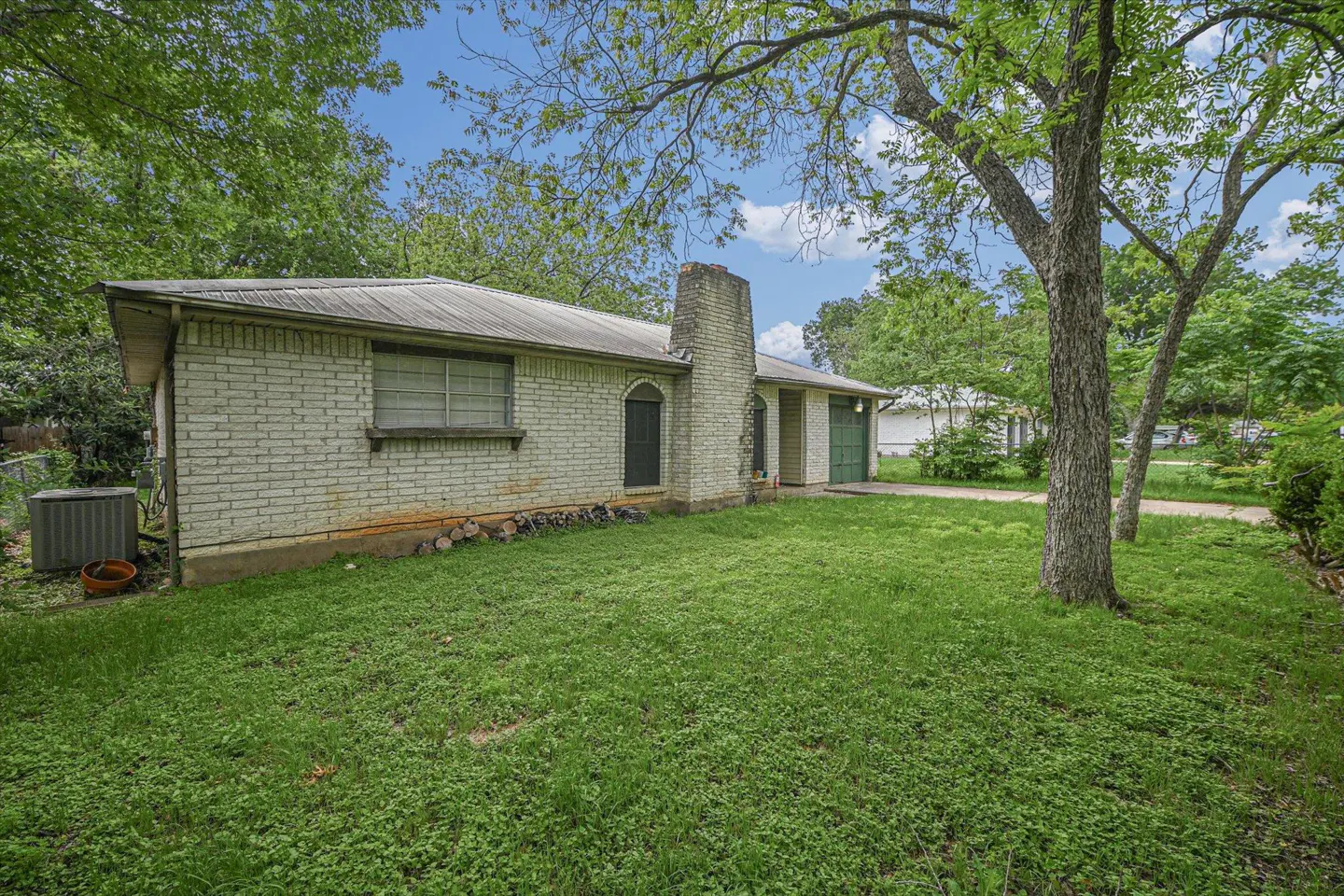 Exterior view of a one-story white brick house with a chimney, green garage door, and a green lawn.
