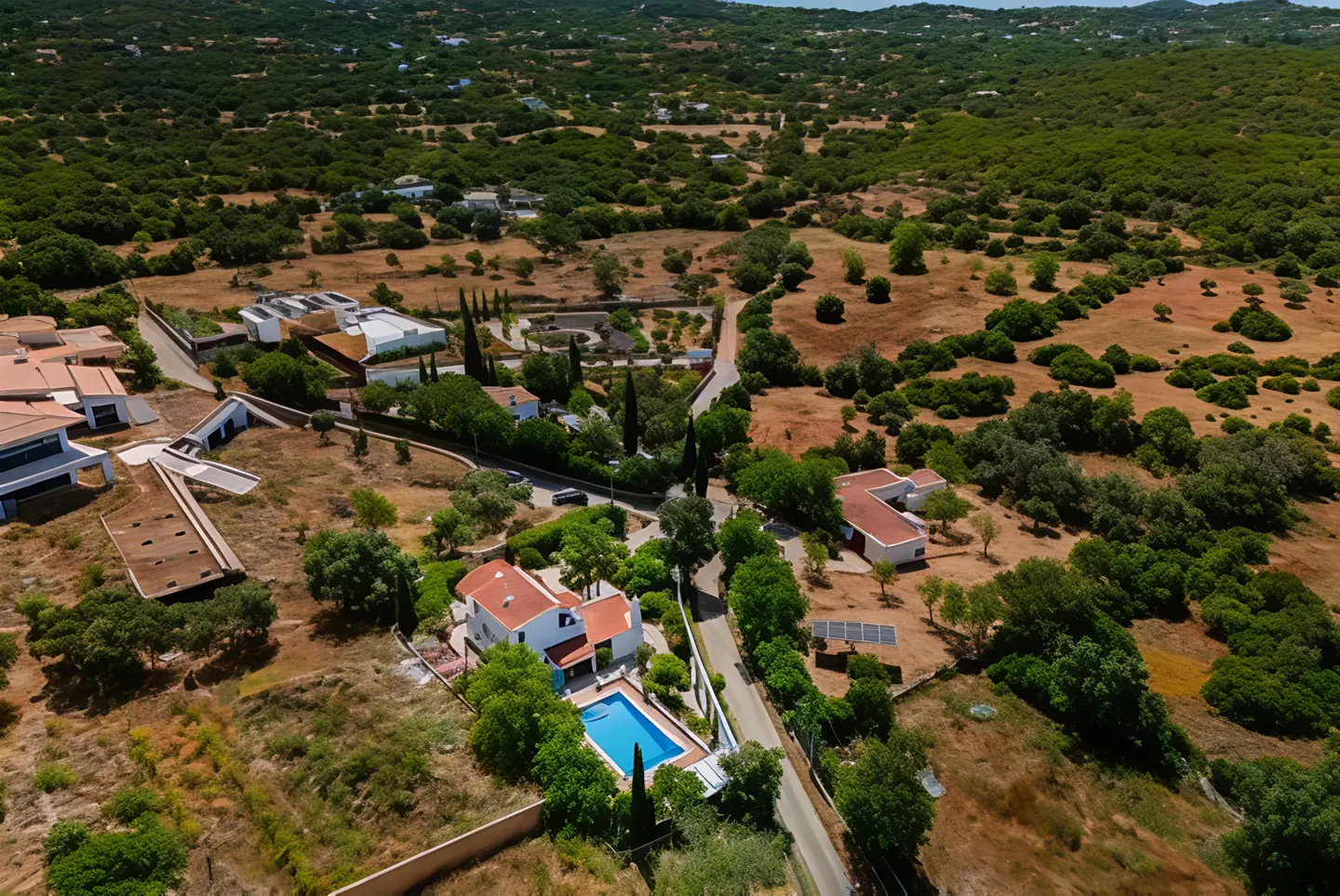 Aerial view of luxury homes with pools and red tile roofs nestled in a green, hilly landscape.
